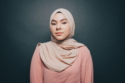 Portrait of confident young woman wearing hijab against gray background