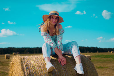 A beautiful young ukrainian woman is sitting on a hay bale smiling