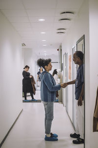 Side view of male healthcare expert shaking hands with female patient standing in corridor