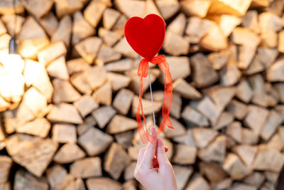 A red heart on a stick is held by a woman's hand. firewood background