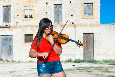 Woman playing violin while standing against building