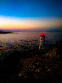 Lighthouse by sea against sky during sunset