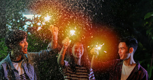 Happy friends holding sparklers at night