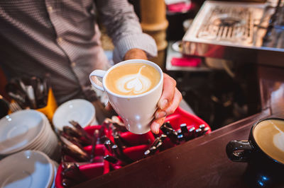 Midsection of barista pouring coffee in cup from container at cafe