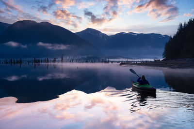 Reflection of man in lake against sky during sunset