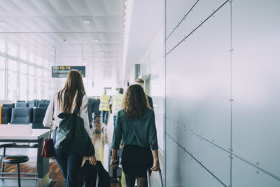 Tear view of multi-ethnic colleagues pulling luggage while walking by wall at airport