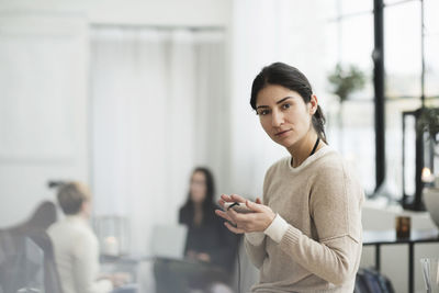 Portrait of businesswoman holding mobile phone with colleagues in background