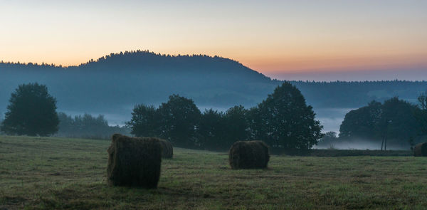 Hay bales on field against sky during sunset