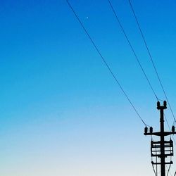 Low angle view of silhouette electricity pylon against clear blue sky