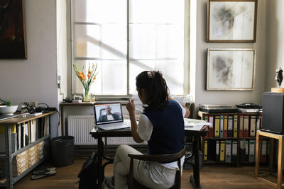 Businesswoman showing document on video call to male colleague at workplace