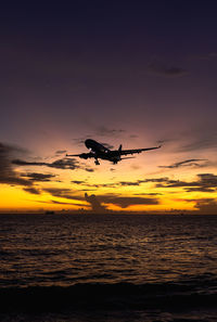 Silhouette airplane flying over sea against sky during sunset