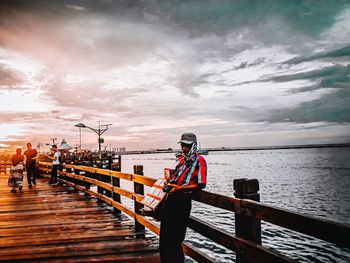 Man sitting on pier over sea against sky during sunset