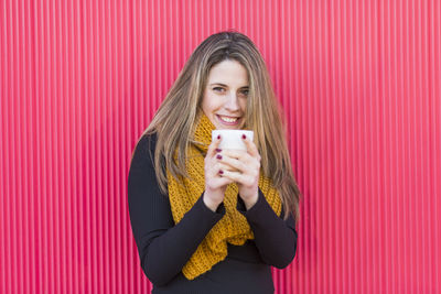 Portrait of smiling woman standing against red wall