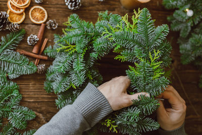 Top view of the hands of a male florist making a christmas wreath from natural materials.