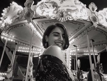 Portrait of smiling young woman against carousel at night