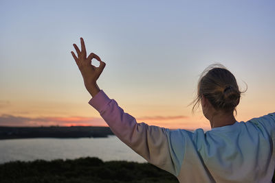 Side view of man with arms raised against sky during sunset