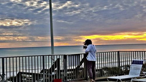 Man standing by railing against sea during sunset