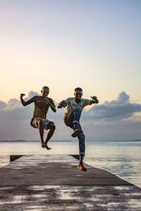 Full length of two men jumping on beach against clear sky during sunset