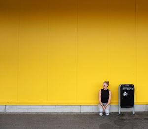 Portrait of woman sitting on yellow wall