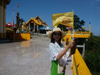 Portrait of smiling woman wearing hat and sunglasses at temple during sunny day