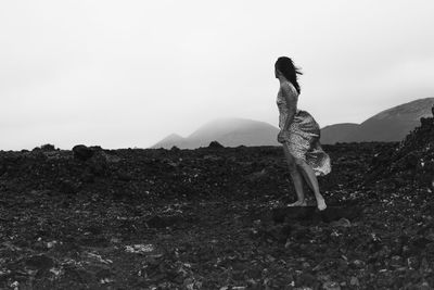 Side view of woman standing on volcanic rocks against sky