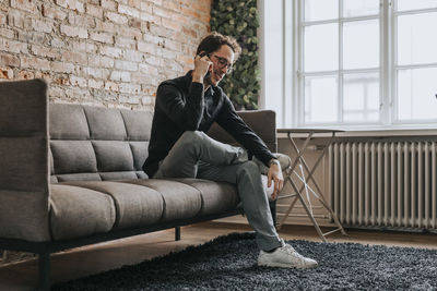 Smiling businessman talking on smart phone while sitting on sofa at office