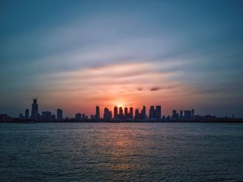 Sea by buildings against sky during sunset