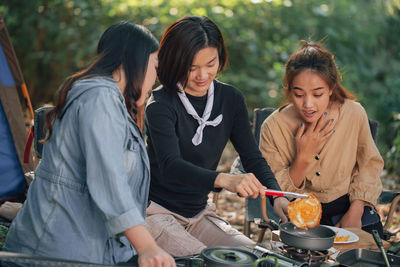 Women and her friend cooking fried egg on stove for dinner at outdoor together, camping concept