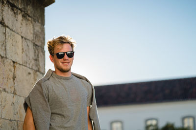 Portrait of young man wearing sunglasses standing against clear sky