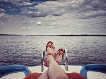 Low section of woman relaxing on boat in river against cloudy sky