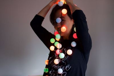 Portrait of smiling woman holding christmas lights standing against wall