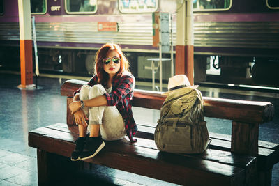 Portrait of young woman sitting on bench at railroad station platform