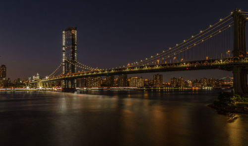 Illuminated bridge over river with city in background