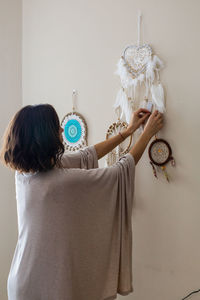 Rear view of woman holding ice cream hanging against wall at home