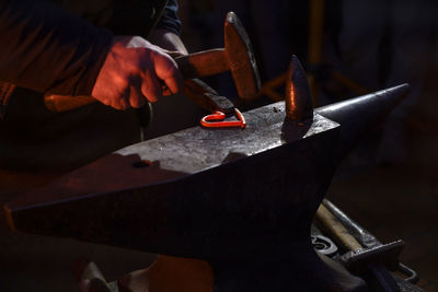 Midsection of blacksmith hammering heart shaped metal in workshop