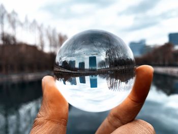 Cropped hand holding crystal ball with reflection of lake and buildings