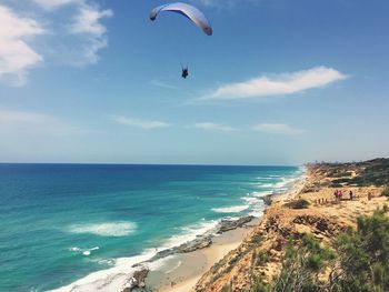 Person paragliding over beach against sky