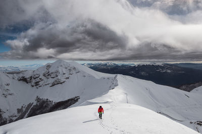 Man climbing on snowcapped mountain against sky