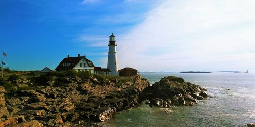 Lighthouse amidst sea and buildings against sky