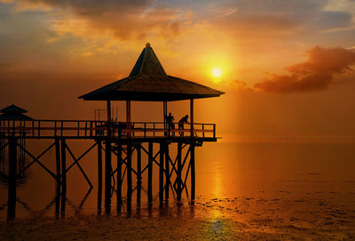 Gazebo in sea against sky during sunset