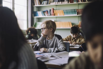 Pupil with hand on chin sitting at desk in classroom