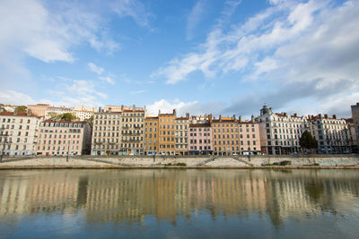 Buildings by river against sky in city