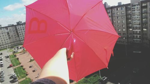 Cropped image of person holding pink umbrella against buildings in city