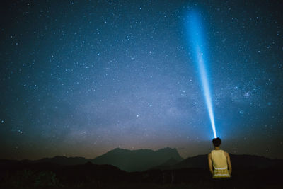 Rear view of man standing on mountain against star field