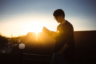 A young asian man looking at camera he is holding while the sun is setting. silhouette photographer.