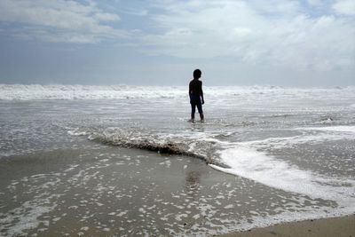 Rear view of man walking on beach against sky