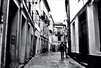 Rear view of man walking on footpath amidst buildings