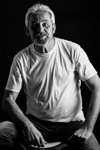 Portrait of man sitting against black background