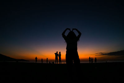 Silhouette people on beach against sky during sunset