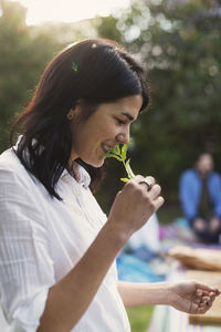 Side view of happy young woman smelling herb while preparing food in backyard